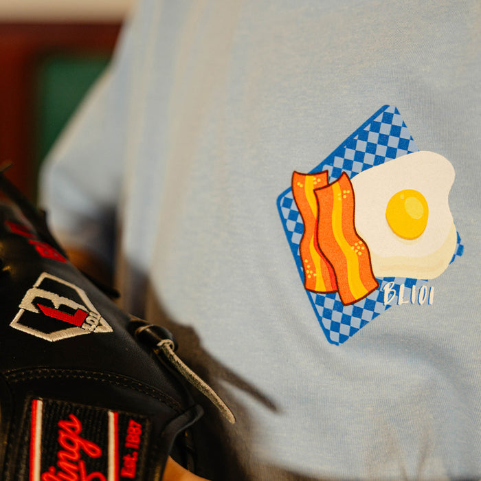 Close up of light blue t-shirt with a bacon and egg graphic on a blurred background