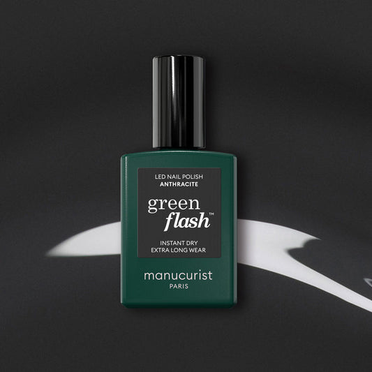 Manucurist’s Anthracite gel polish, a lustrous dark grey shade, is displayed on a black surface with white abstract highlights.