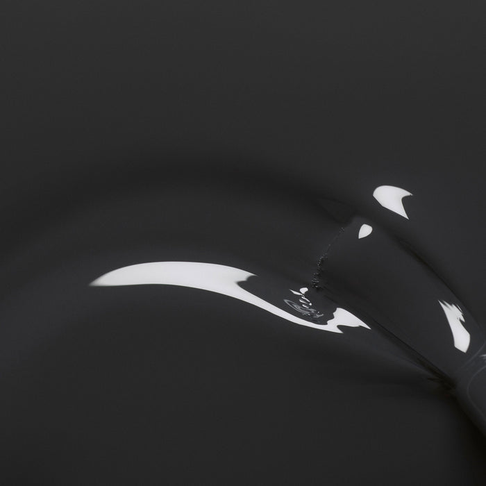 A close-up of Anthracite by Manucurist shows a black, glossy surface with smooth curves and white reflections, evoking dark grey nail polish for an abstract, minimalist effect.