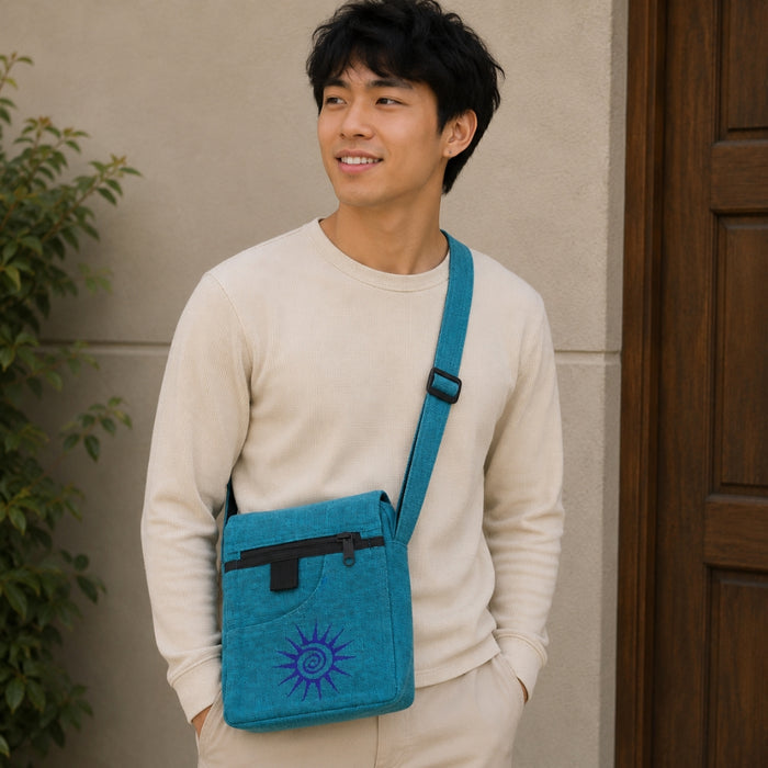 Man wearing a blue crossbody bag with a sun design, standing against a beige wall.