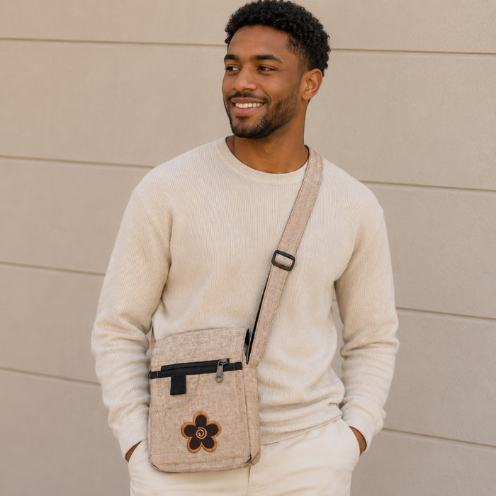 Man wearing a beige sweater and carrying a matching crossbody bag against a beige wall.