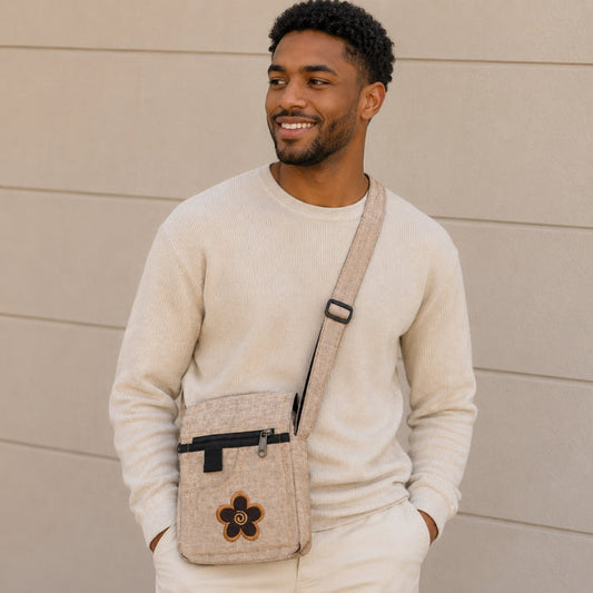 Man wearing a beige sweater and carrying a matching crossbody bag against a beige wall.