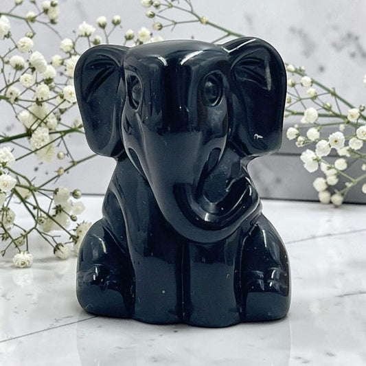 Black elephant crystal on a marble surface with white flowers in the background