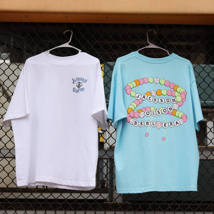 White and light blue Jackson Olson x BL101 relaxed tees hanging on a chain-link fence, showing front and back graphic details side by side