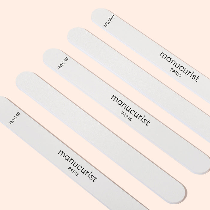 Five Manucurist-us 180/240 emery boards for fragile nails are arranged diagonally on a light beige background, ideal for gently shaping brittle or sensitive nails.