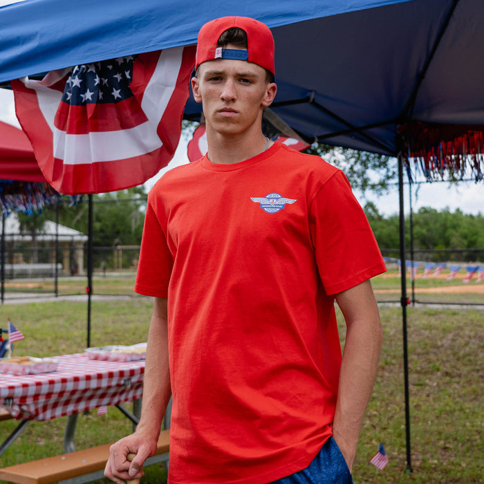 Fastball Flight Tee - Red: Front-facing adult male model wearing red Fastball Flight tee at outdoor baseball event