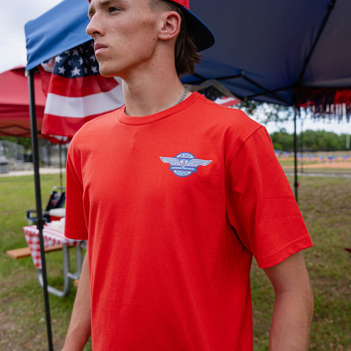 Close-up of adult male model in red Fastball Flight tee showing Air Show Division badge on chest at outdoor event