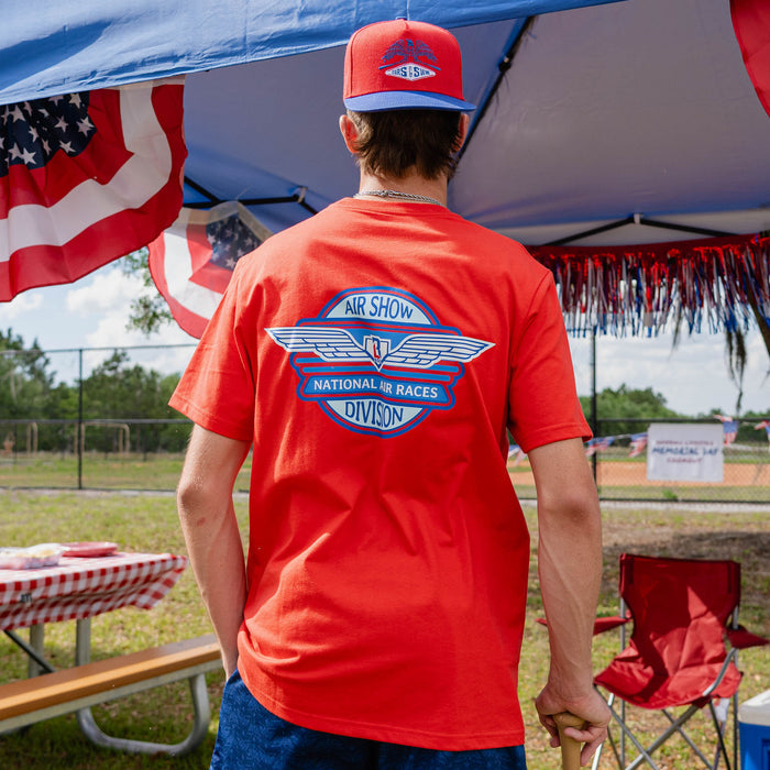 Fastball Flight Tee - Red: Back view of adult male model showing Air Show National Air Races Division badge on red tee at outdoor baseball event