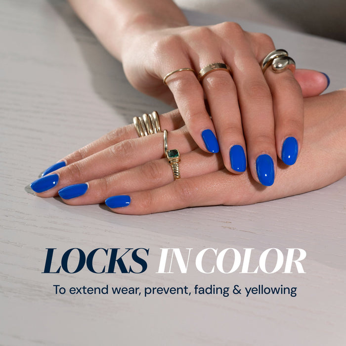 Close-up of hands with bright blue nail polish and rings, resting on a white surface. Text reads: "LONDONTOWN Flash Dry Top Coat locks in color with a fast-dry finish to extend wear, prevent fading & yellowing.