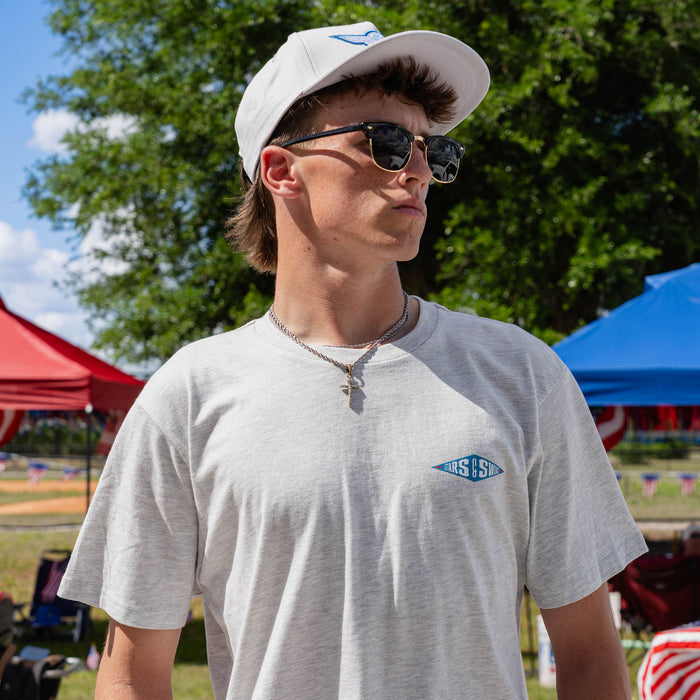 Close-up of adult male model wearing heather gray Freedom Swings tee with Stars and Swings logo visible on chest at outdoor event