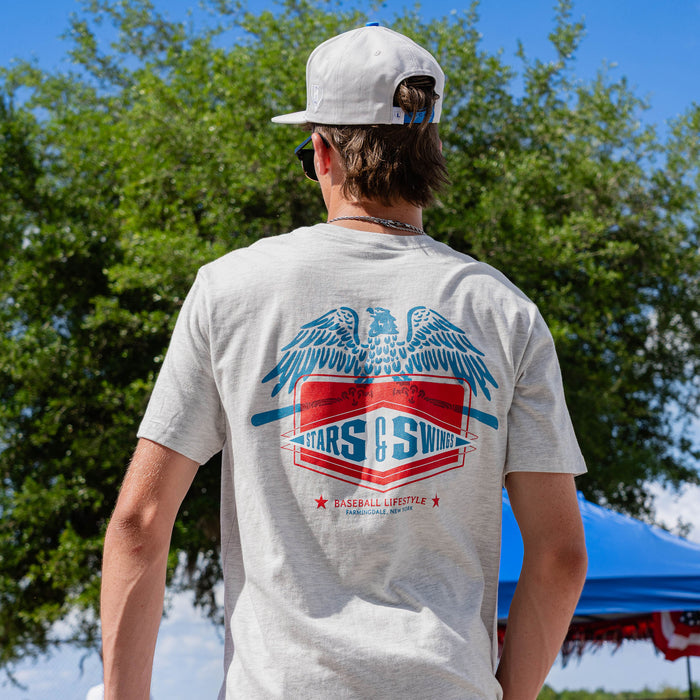 Back view of adult male model showing Stars and Swings eagle graphic on heather gray tee at outdoor baseball event