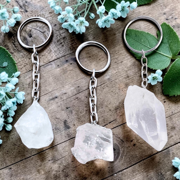 Three crystal keychains on a wooden surface with green leaves and flowers.