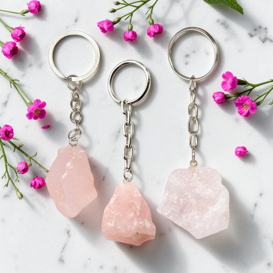Three Rose Quartz keychains on a marble surface with pink flowers.