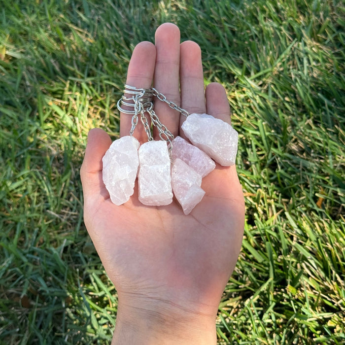 Hand holding Rose Quartz keychains against a grass background