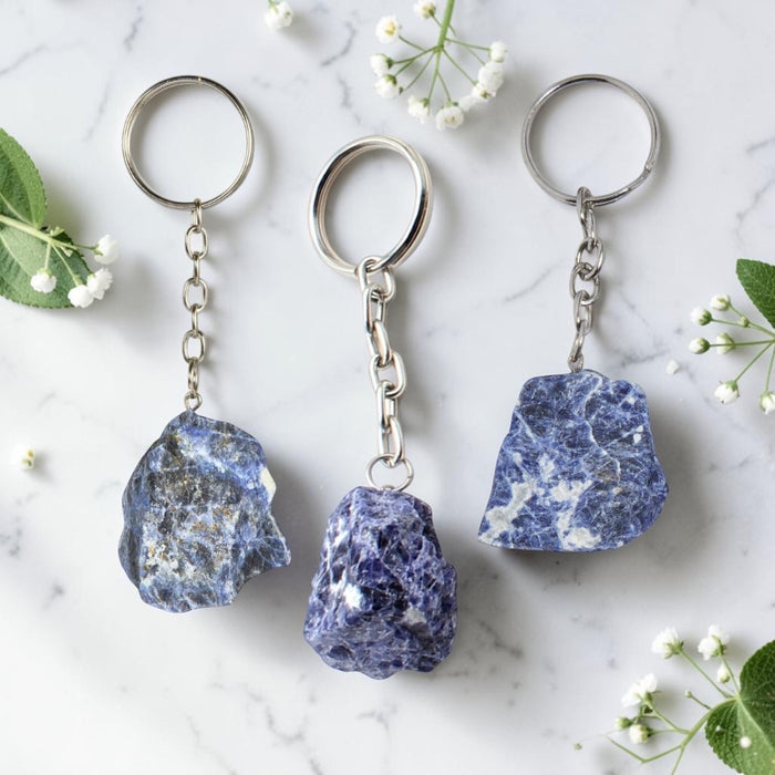 Three keychains with natural stone pendants on a marble surface with flowers.
