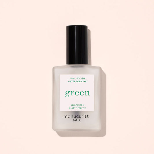 A frosted glass bottle of Manucurist Matte Top Coat with a black cap, ideal for a plant-based manicure, sits against a light beige background. The label features "Quick Dry Matte Effect.