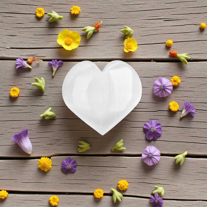 White selenite heart surrounded by colorful flowers on a wooden surface