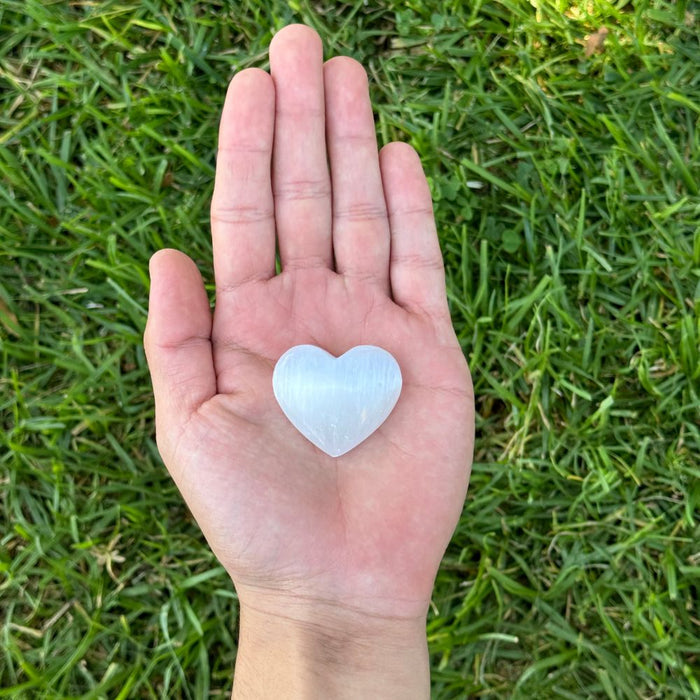 Heart-shaped selenite held in a hand against a grass background